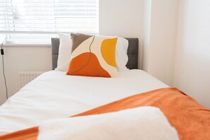 A bed with a white mattress, a grey headboard, and a pillow with abstract patterns. - House Sleeps 7 With Garden (Wolverhampton)