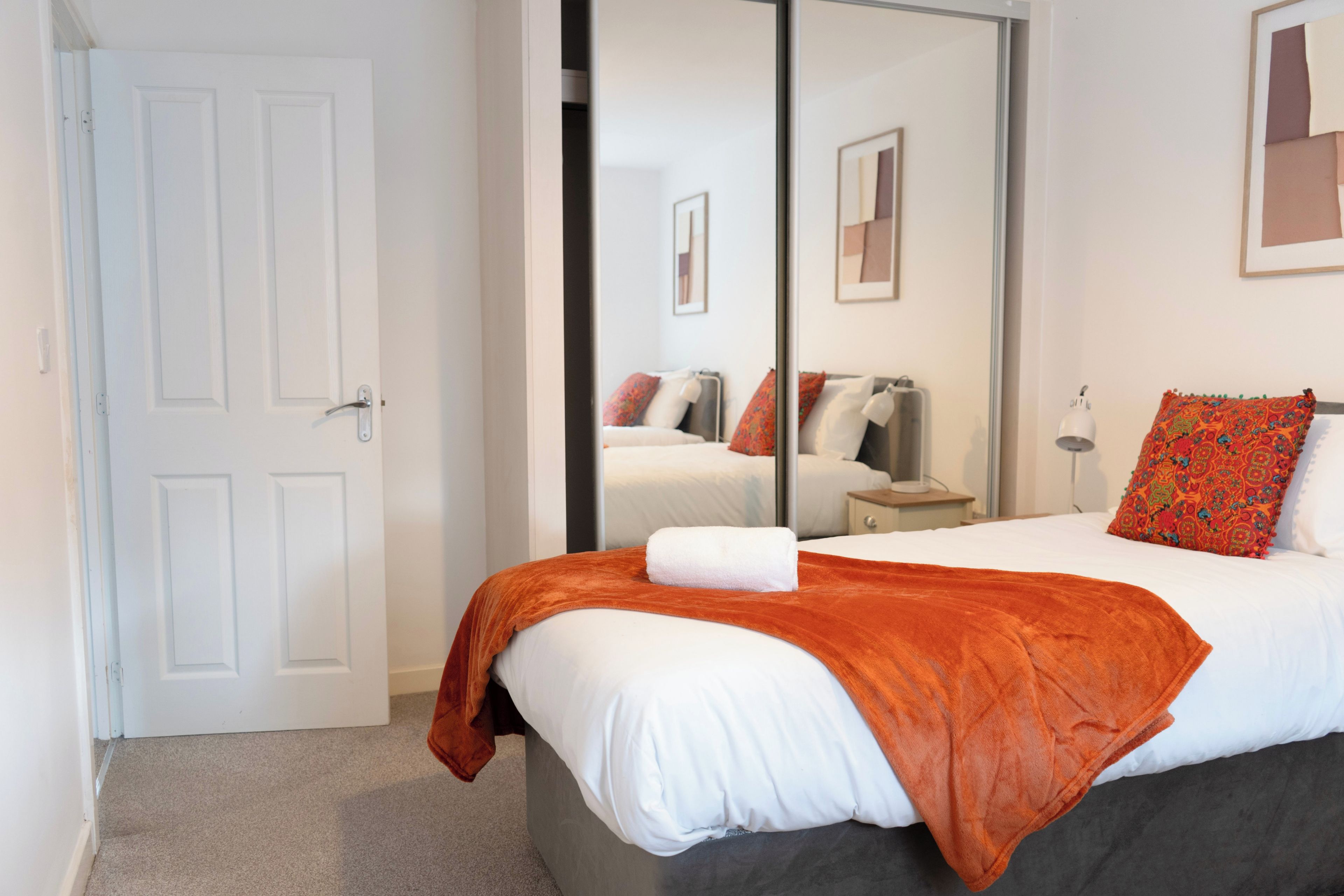 Une chambre d’hôtel avec un lit, une table de chevet, un miroir et une porte.