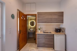 A compact kitchen with a wooden door, a sink, a coffee maker, and a small refrigerator. - Villa Kirianna by Villa Plus (Kirianna)