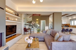 A modern living room with a sectional sofa, a coffee table with flowers, and a TV. - Villa Kirianna by Villa Plus (Kirianna)