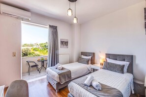 Habitació d'hotel amb dos llits, una taula petita amb una cadira, vista a l'exterior i un ventilador de sostre.