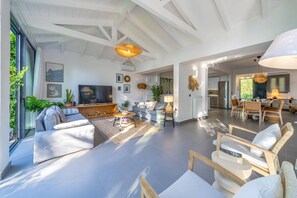 Un amplio espacio de sala con un televisor grande, asientos cómodos y una cocina al fondo.
