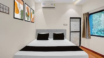 Una habitación de hotel moderna con una cama grande, obras de arte enmarcadas en la pared, un equipo de aire acondicionado y una ventana con vistas a zonas verdes.