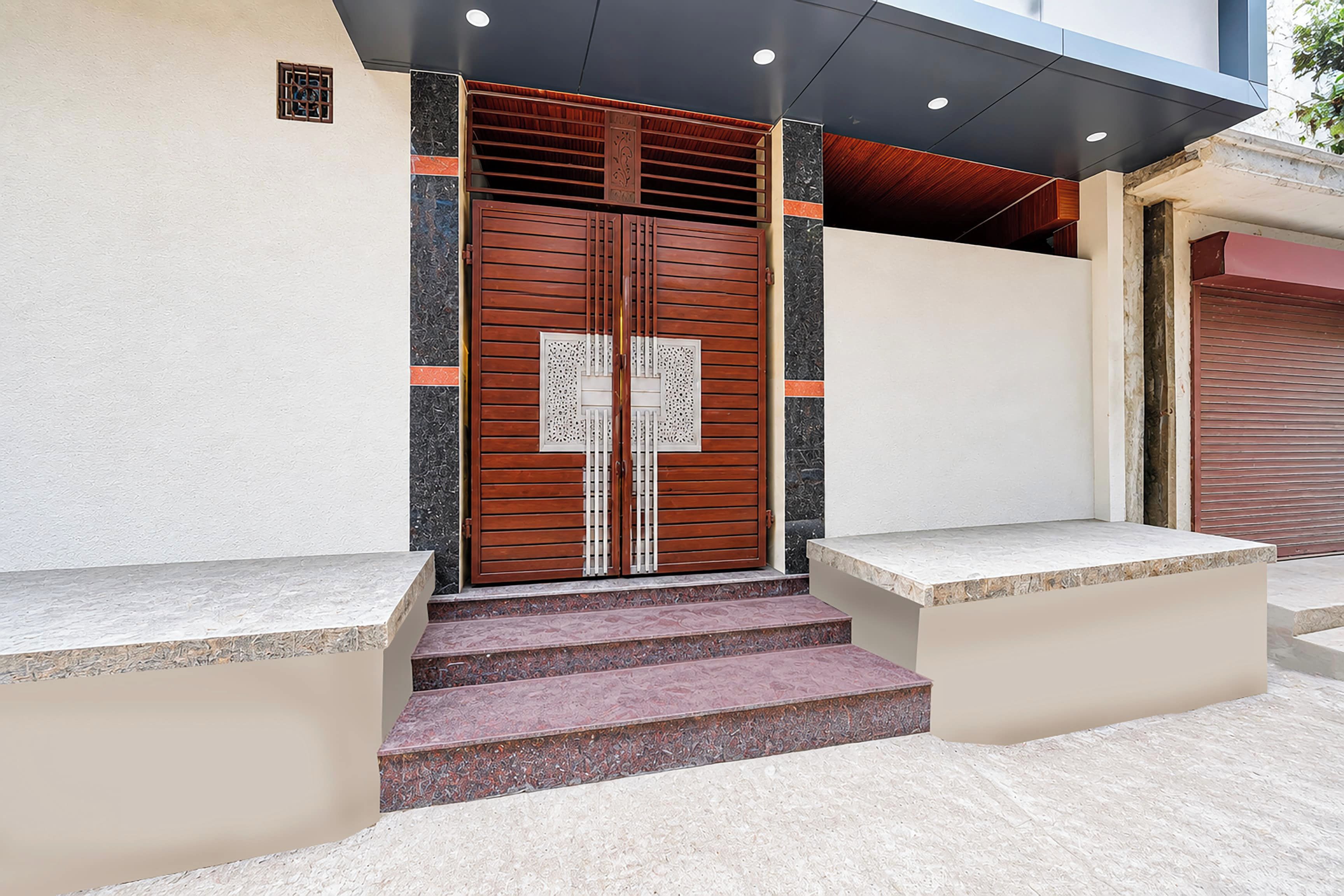 Entrada de un edificio con una puerta de madera doble, escalones que conducen a ella y un pequeño alero superior.