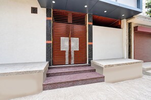 Entrada de un edificio con una puerta de madera doble, escalones que conducen a ella y un pequeño alero superior.
