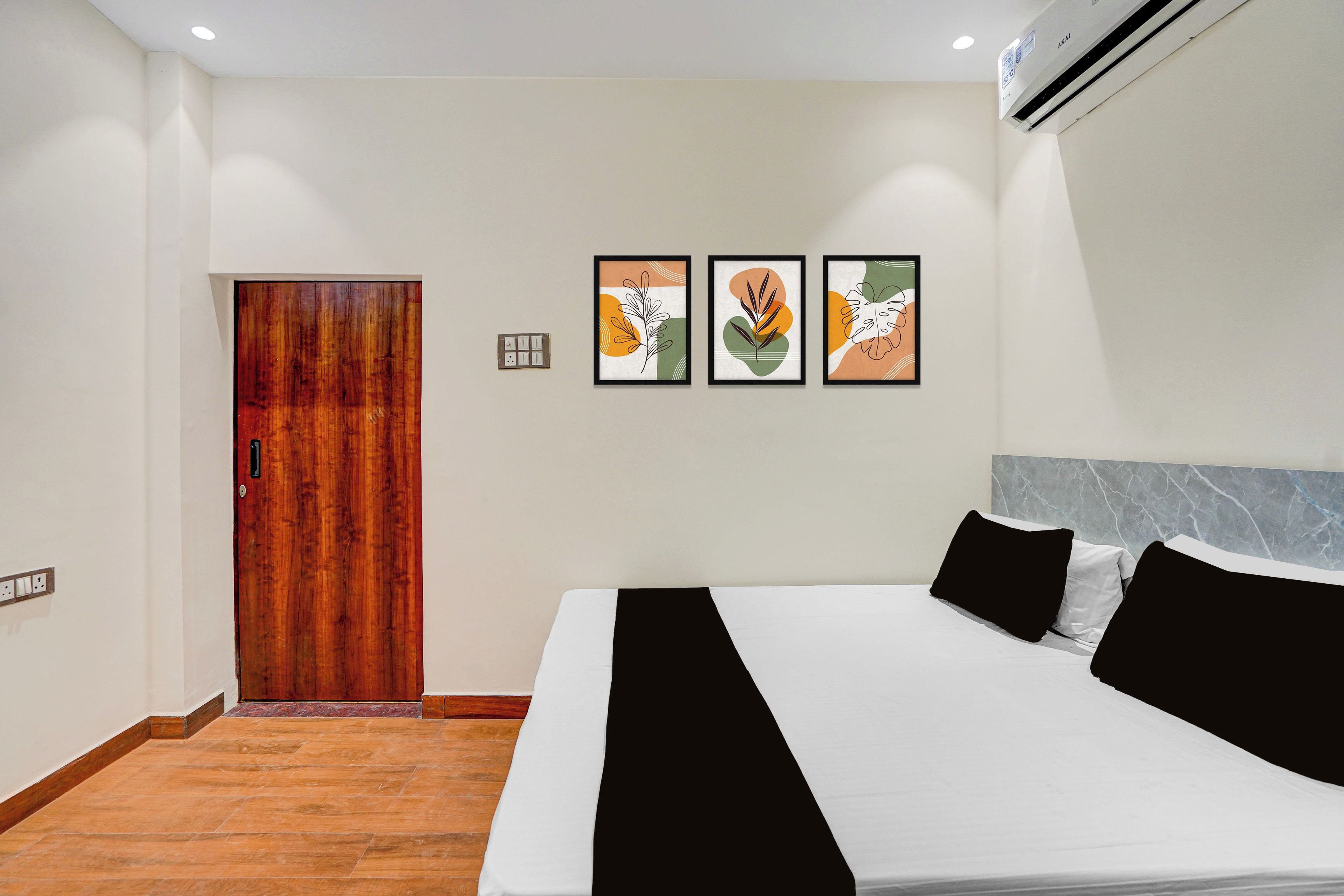 Quarto de hotel com porta de madeira, cama com roupa de cama preta e branca, e três obras de arte emolduradas na parede.