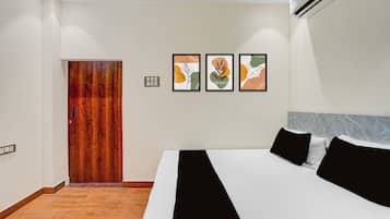 Quarto de hotel com porta de madeira, cama com roupa de cama preta e branca, e três obras de arte emolduradas na parede.