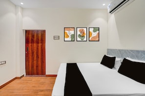 A hotel room with a wooden door, a bed with black and white bedding, and three framed artworks on the wall. - Hotel O Kali Ghat Prayagraj (Prayagraj)