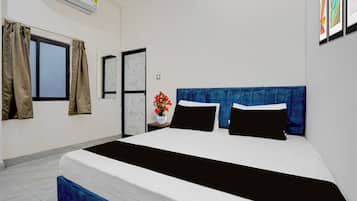 Ein Hotelzimmer mit Bett, einem fensterbeprägten Bereich mit Vorhängen, einer Tür und einer Wand-Klimaanlage.