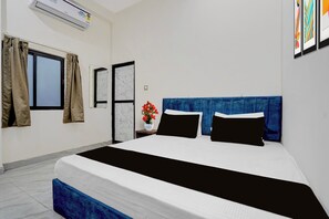 Une chambre d’hôtel avec un lit, une fenêtre avec des rideaux, une porte et un climatiseur fixé au mur.