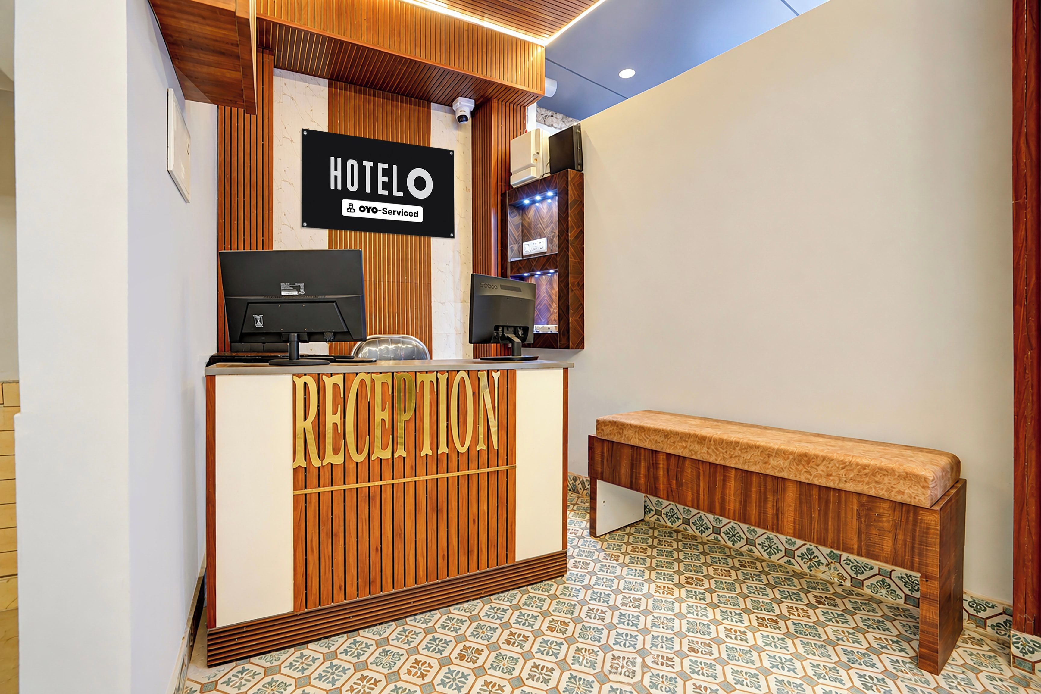 Uma área de recepção de hotel com um balcão de madeira, um banco e uma placa indicando que é administrado pela OYO.