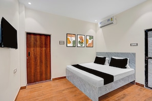 Una camera d'albergo con un letto, una TV a schermo piatto, una porta in legno e opere d'arte alle pareti.