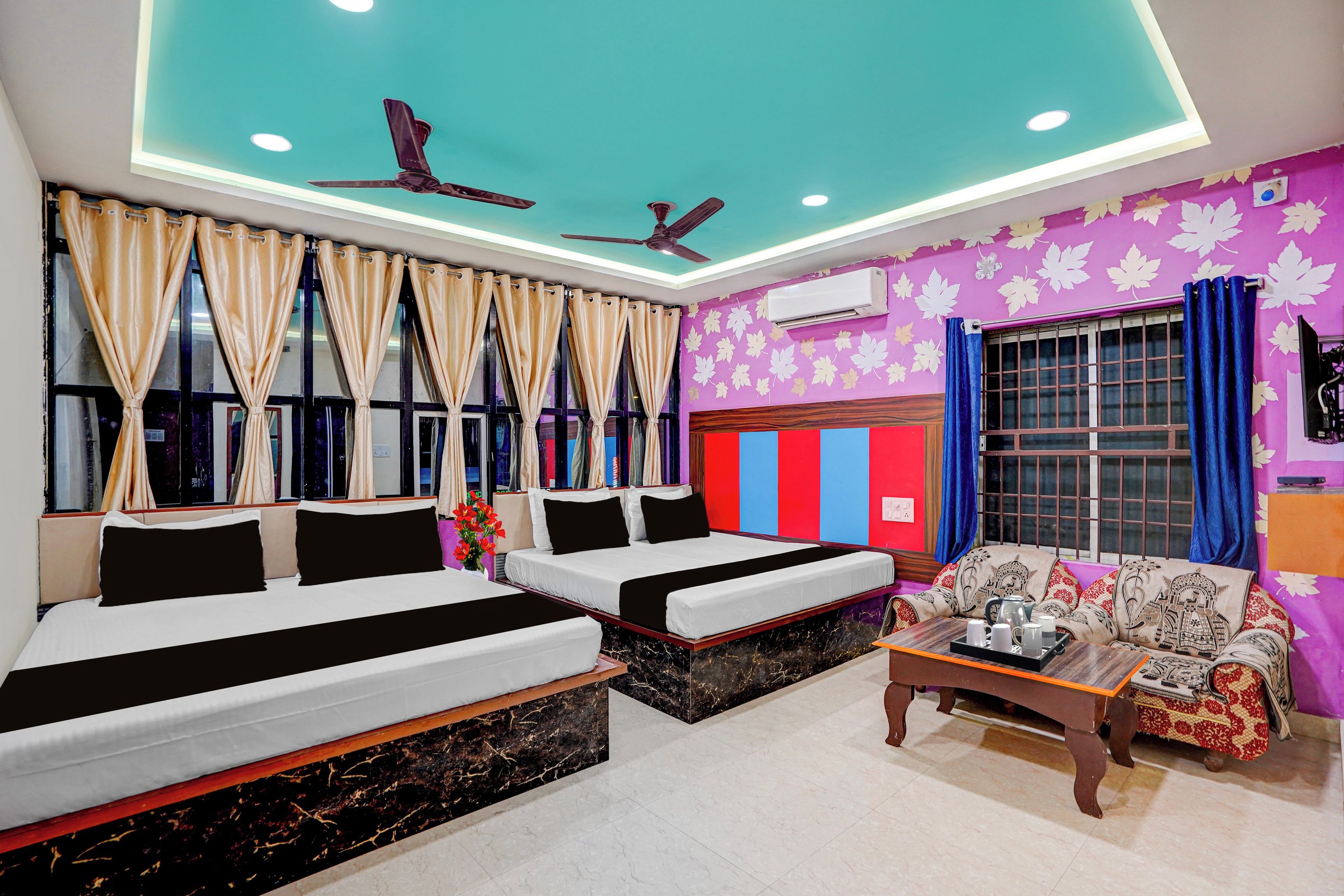 A hotel room with two beds, a sofa, a coffee table, and a ceiling fan.