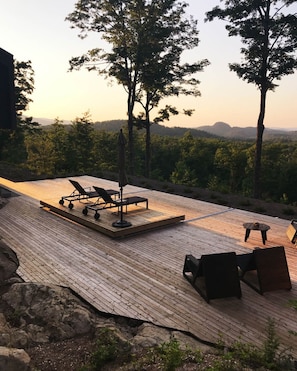 Una terraza al aire libre con sillones de descanso y una mesa, rodeada de árboles y vistas al paisaje.