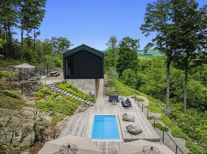A modern outdoor pool area with a wooden deck, lounge chairs, and a black building. - LE BOLTON - Exceptional architect-designed mountain chalet with a pool (Bolton-Est)