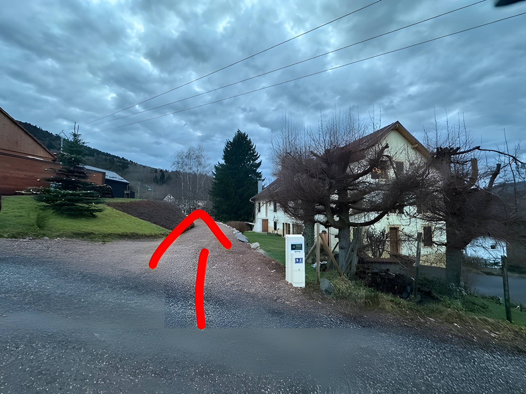 Une route de campagne, avec une maison sur la droite et une grange sur la gauche.