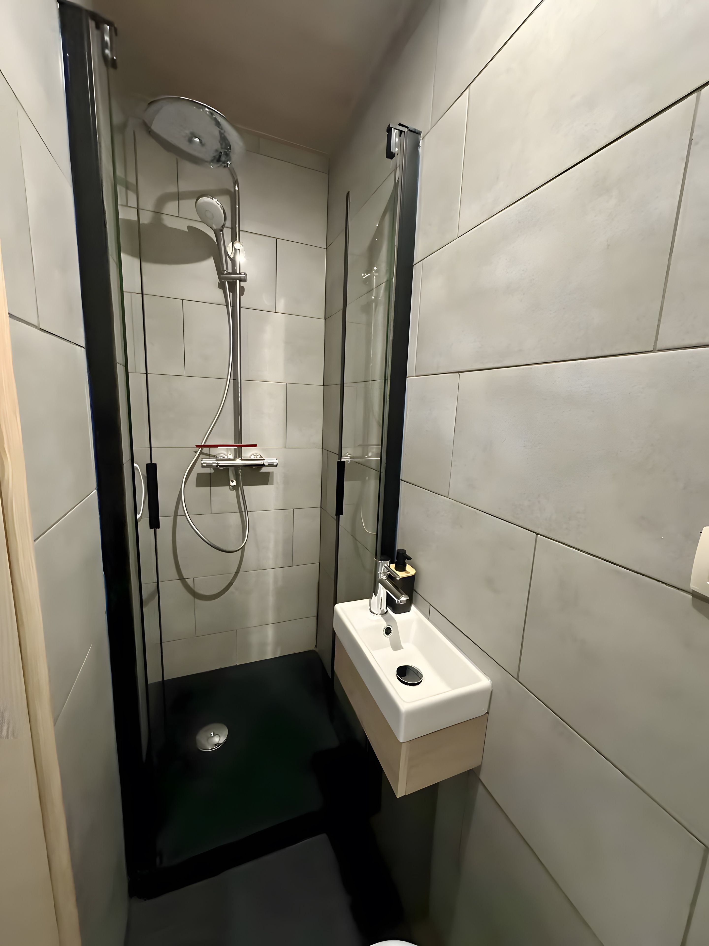 Une salle de bain moderne avec une douche à parois de verre, un lavabo blanc et un tapis de sol noir.