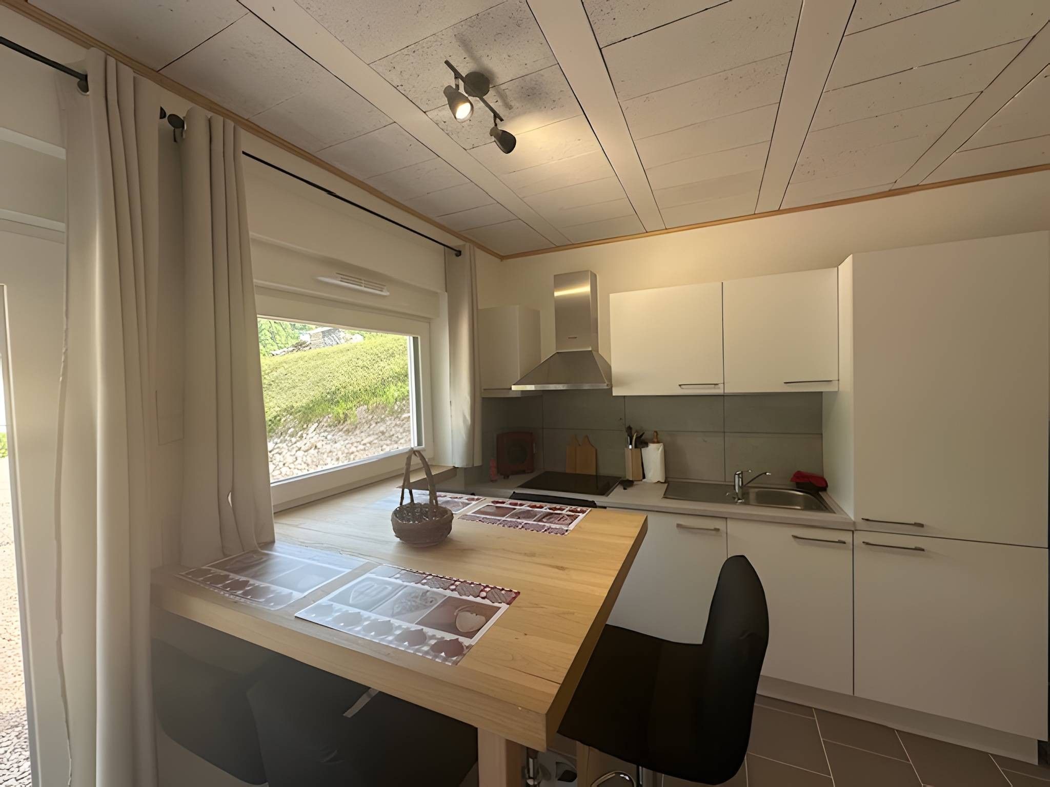 Een kleine keuken met een eethoek, een raam met gordijnen en uitzicht op groen.