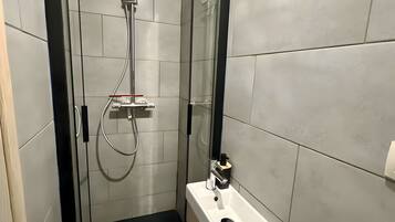 Une salle de bain moderne avec une douche à parois de verre, un lavabo blanc et un tapis de sol noir.
