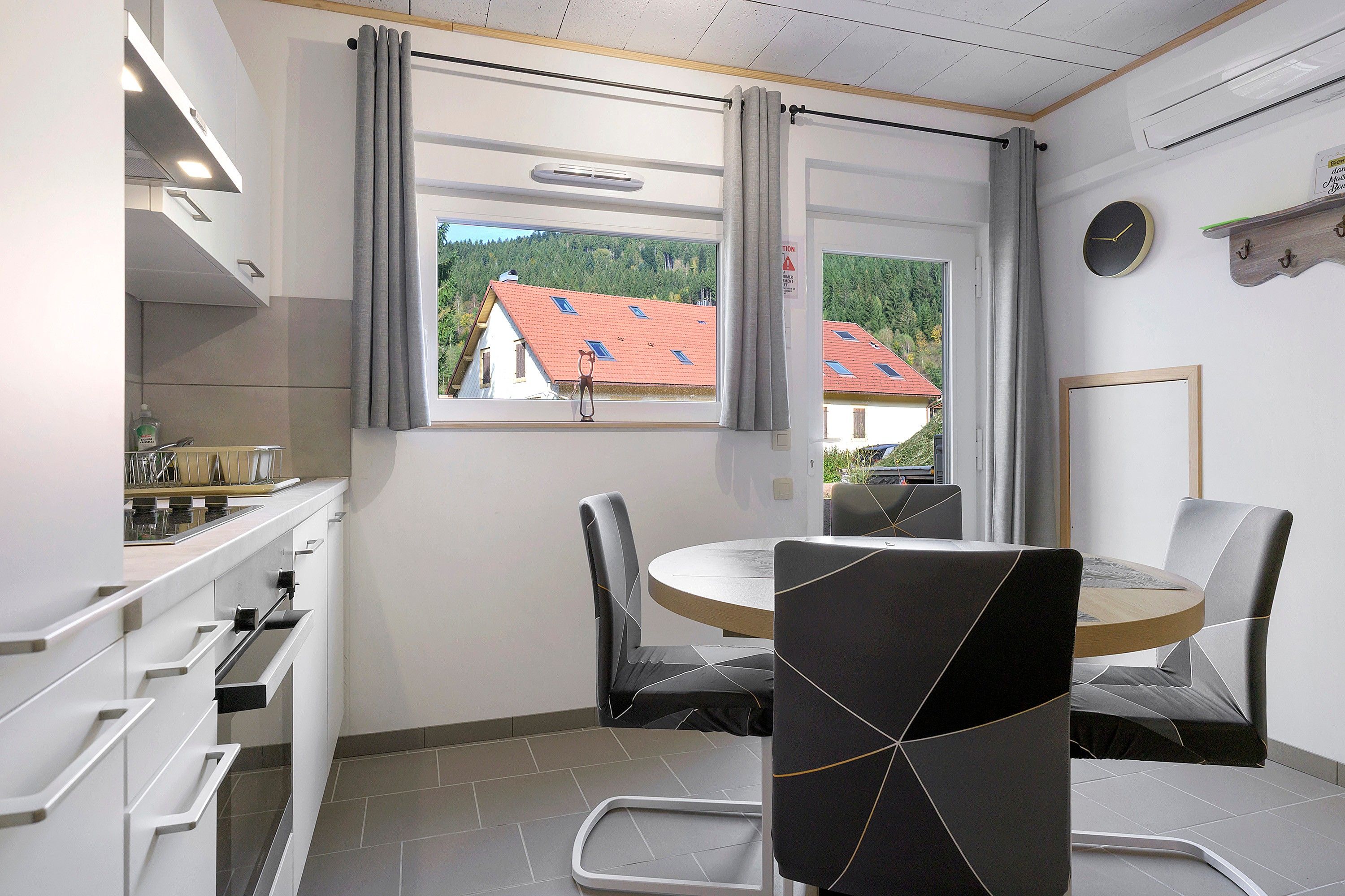 Eine moderne Küche mit Essbereich, Blick auf Häuser durch ein Fenster und einer Uhr an der Wand.