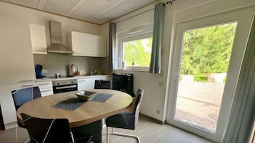 Une cuisine moderne avec un coin repas, de grandes fenêtres et une vue sur la verdure.