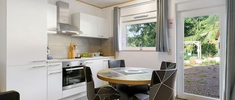 Una cocina moderna con armarios blancos, horno empotrado y comedor con una mesa y sillas redondas.