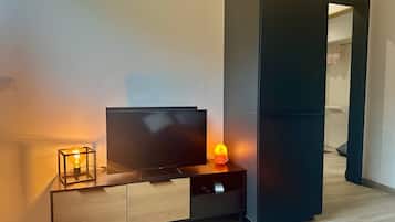 Un salon moderne avec un téléviseur à écran plat posé sur un meuble en bois, une petite table avec une lampe et une porte coulissante sombre.