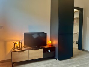 Een moderne woonkamer met een flatscreen televisie op een houten kast, een kleine tafel met een lamp en een donkere schuifdeur.
