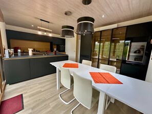 Een moderne keuken met een centraal eiland, een witte eettafel met oranje placemats en hangende lampen.