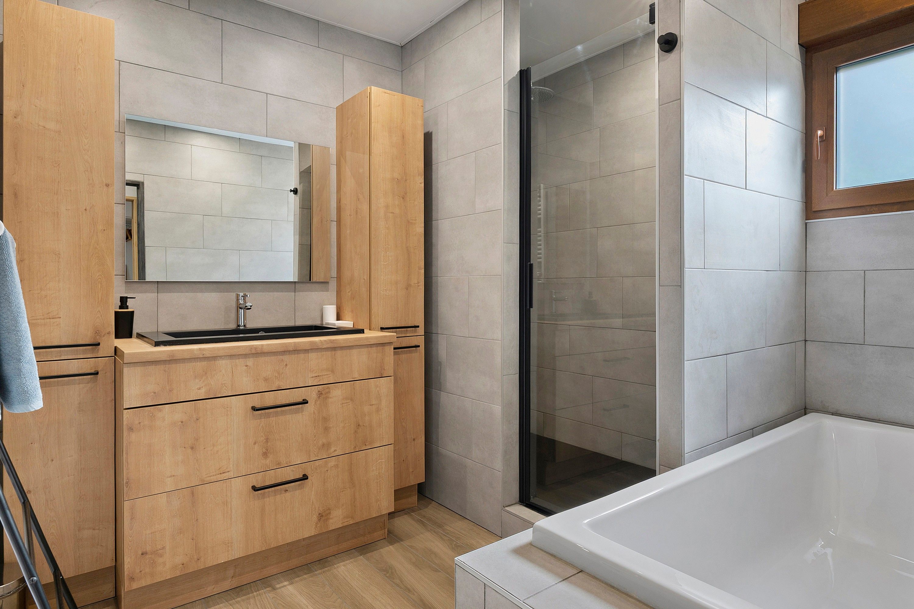 A modern bathroom with a wooden vanity, a glass shower enclosure, and a white bathtub.