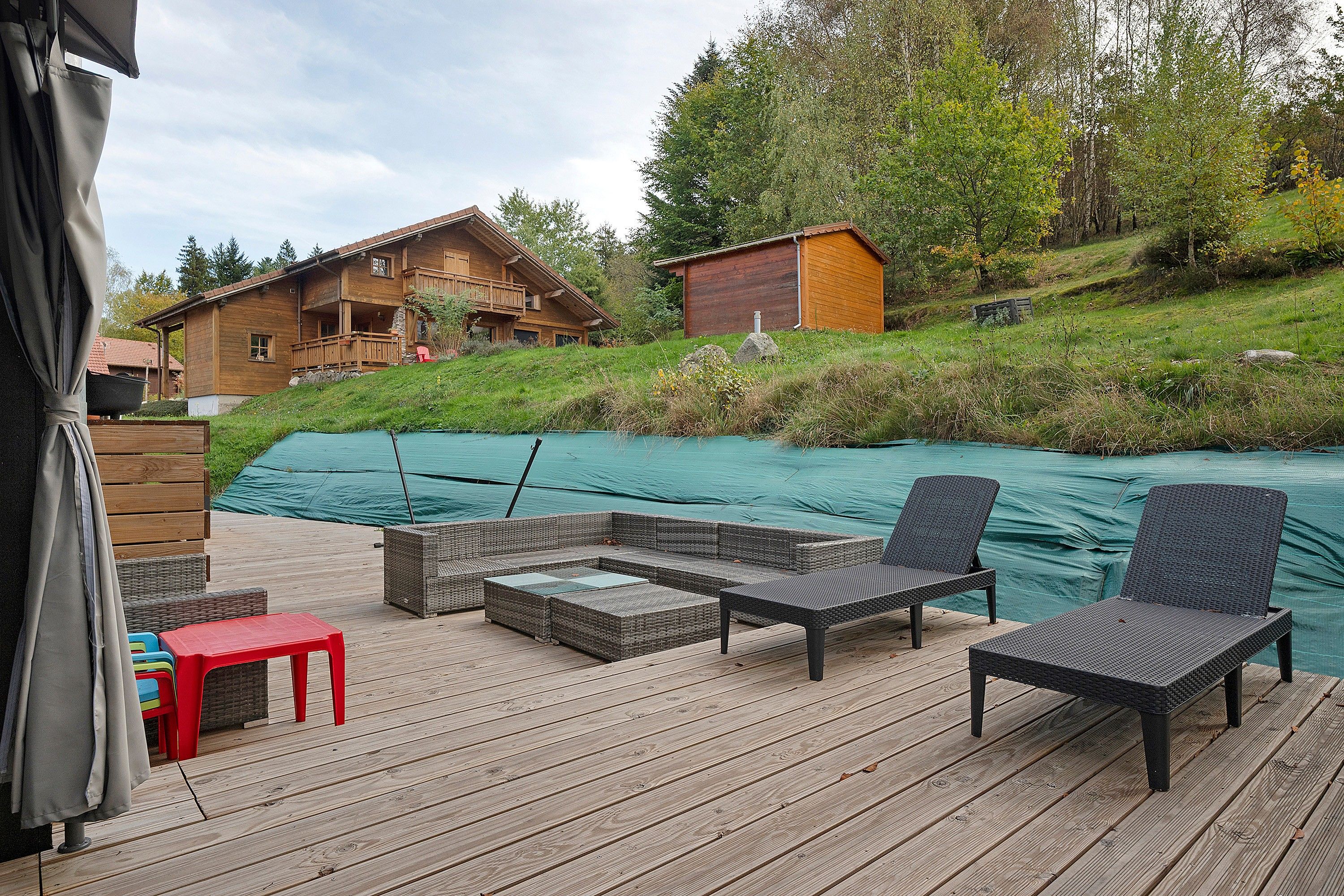 Een houten terras met tuinmeubilair, een zwembad en een houten huis op de achtergrond.