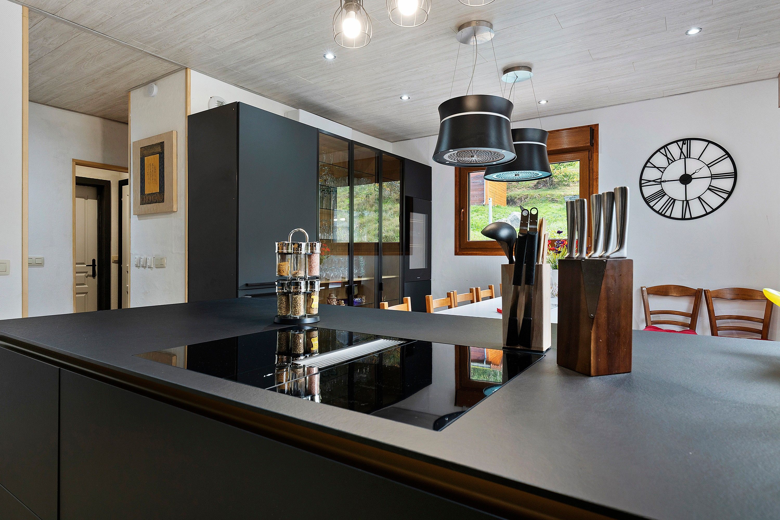 A modern kitchen with a central island, pendant lighting, and a large wall clock.