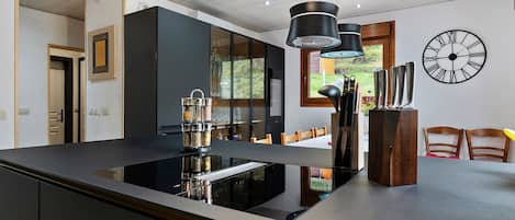 A modern kitchen with a central island, pendant lighting, and a large wall clock.