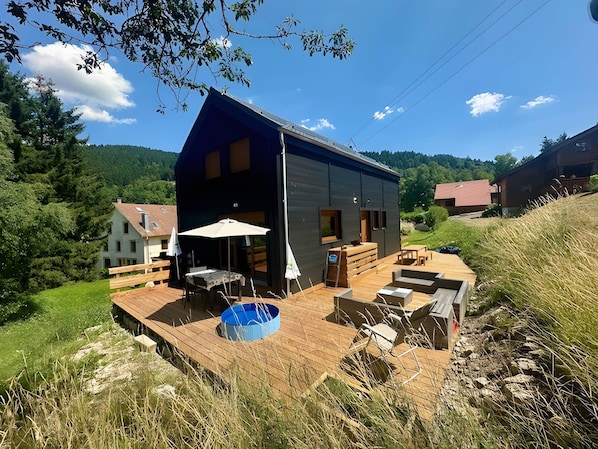 Una casa moderna con una terrazza in legno, arredi da esterno e una piscina.