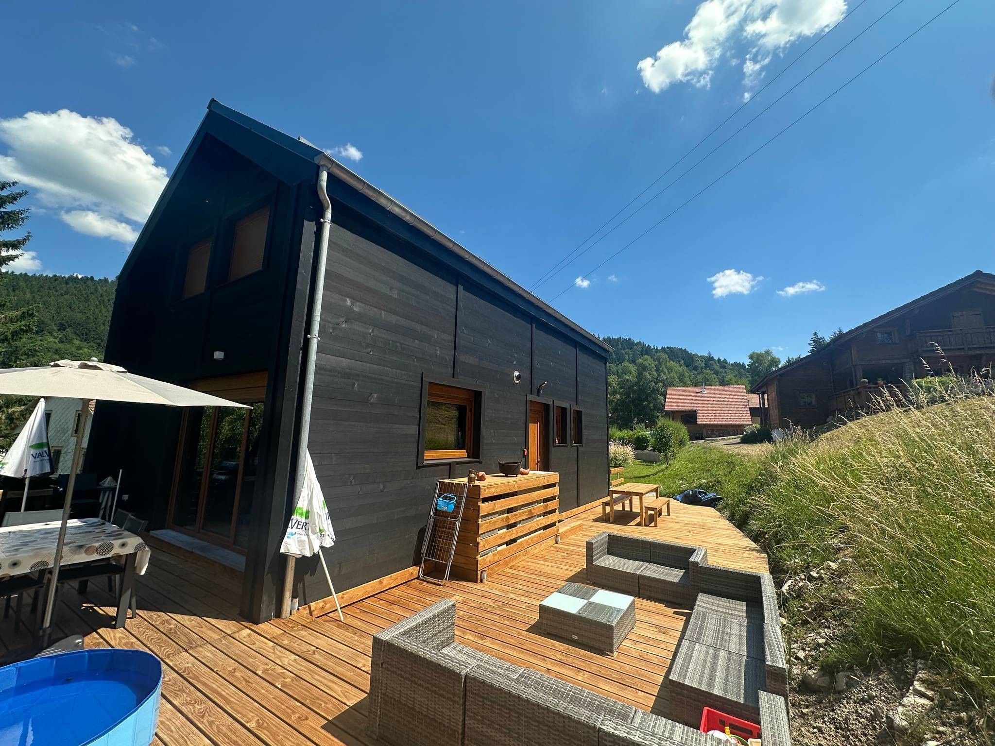 A modern house with a wooden deck, outdoor seating, and a swimming pool.