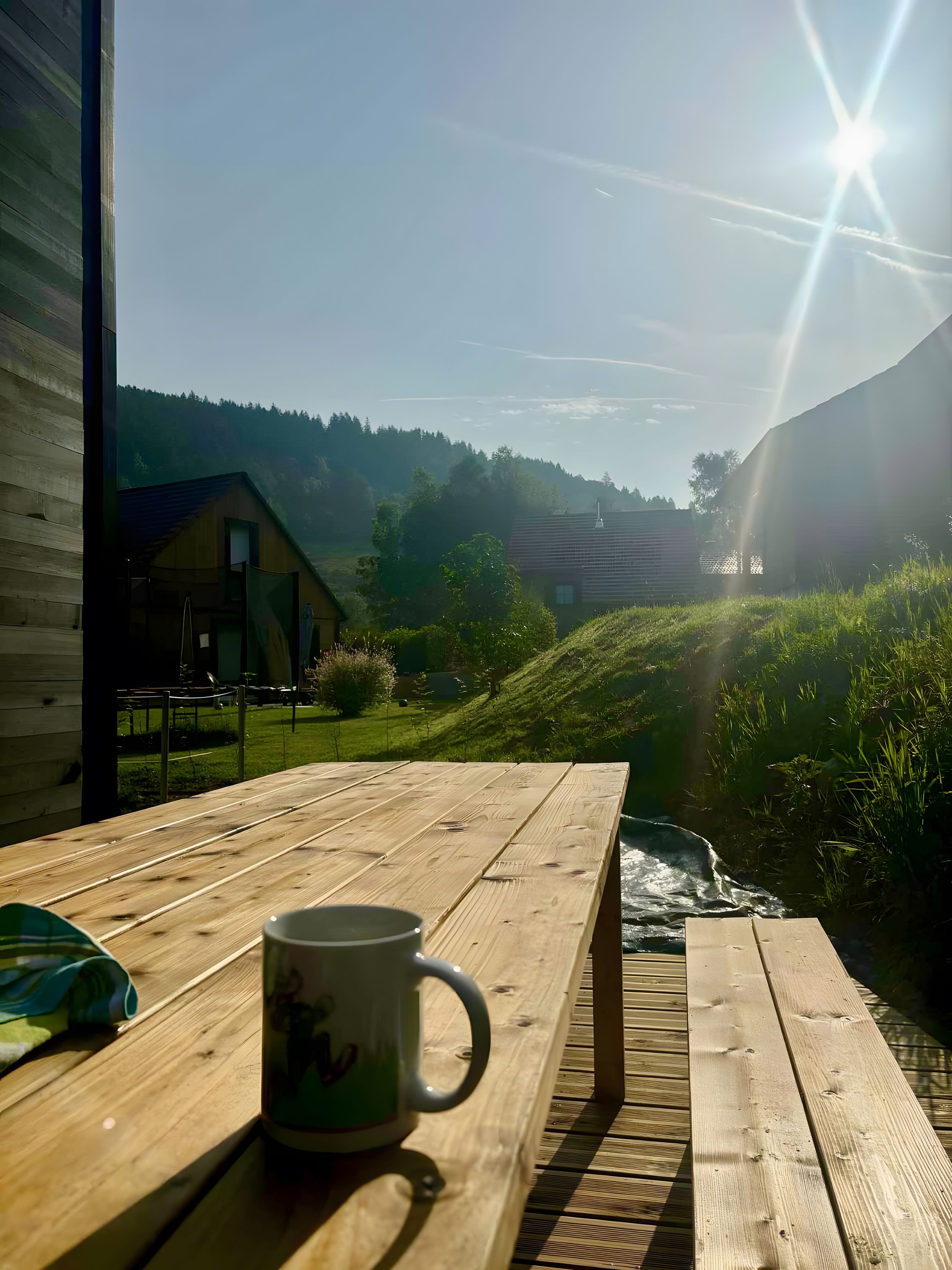 Ein Holztisch mit einer Tasse, mit Blick auf einen Fluss und Häuser in einem Tal.