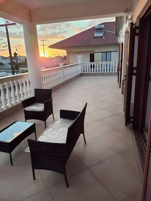 Ein Balkon mit Blick auf einen Sonnenuntergang, mit Fliesenboden, Korbmöbeln und einem Geländer.