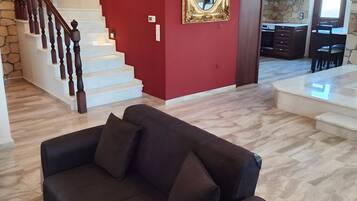 Ein Wohnzimmer mit einem dunkelgrauen Sofa, einer Treppe mit Holzspindeln, einer roten Akzentwand und einem großen Spiegel.