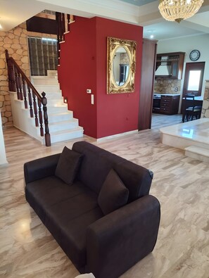 Ein Wohnzimmer mit einem dunkelgrauen Sofa, einer Treppe mit Holzspindeln, einer roten Akzentwand und einem großen Spiegel.