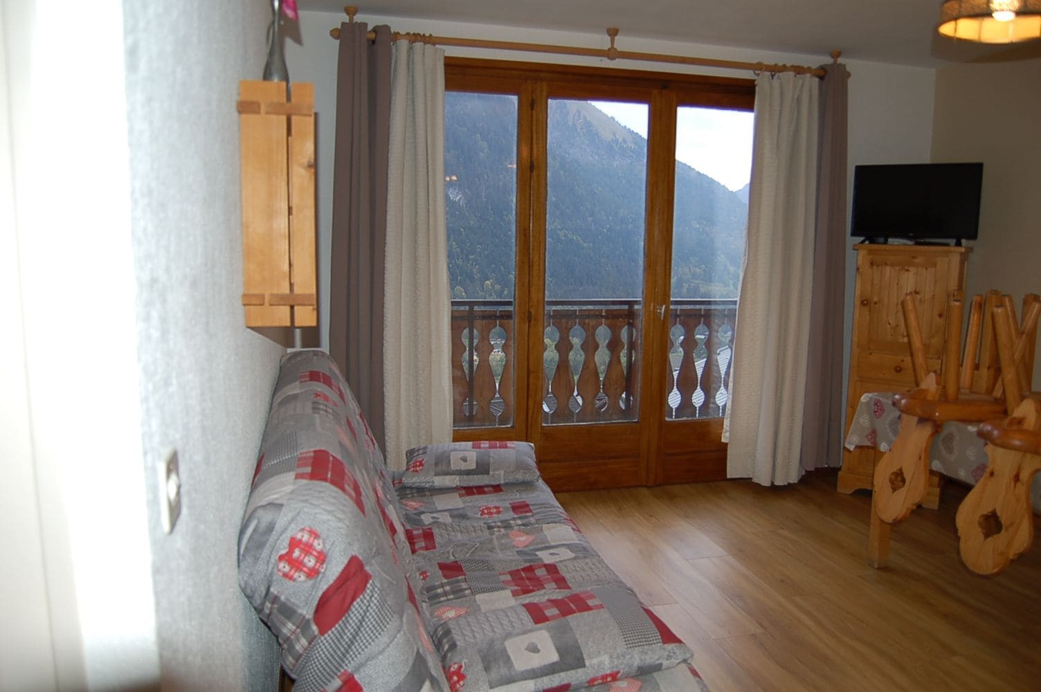 Ein Zimmer mit einer Sitzecke, Holzstühlen, einem Fernseher und einem Balkon mit Bergblick.