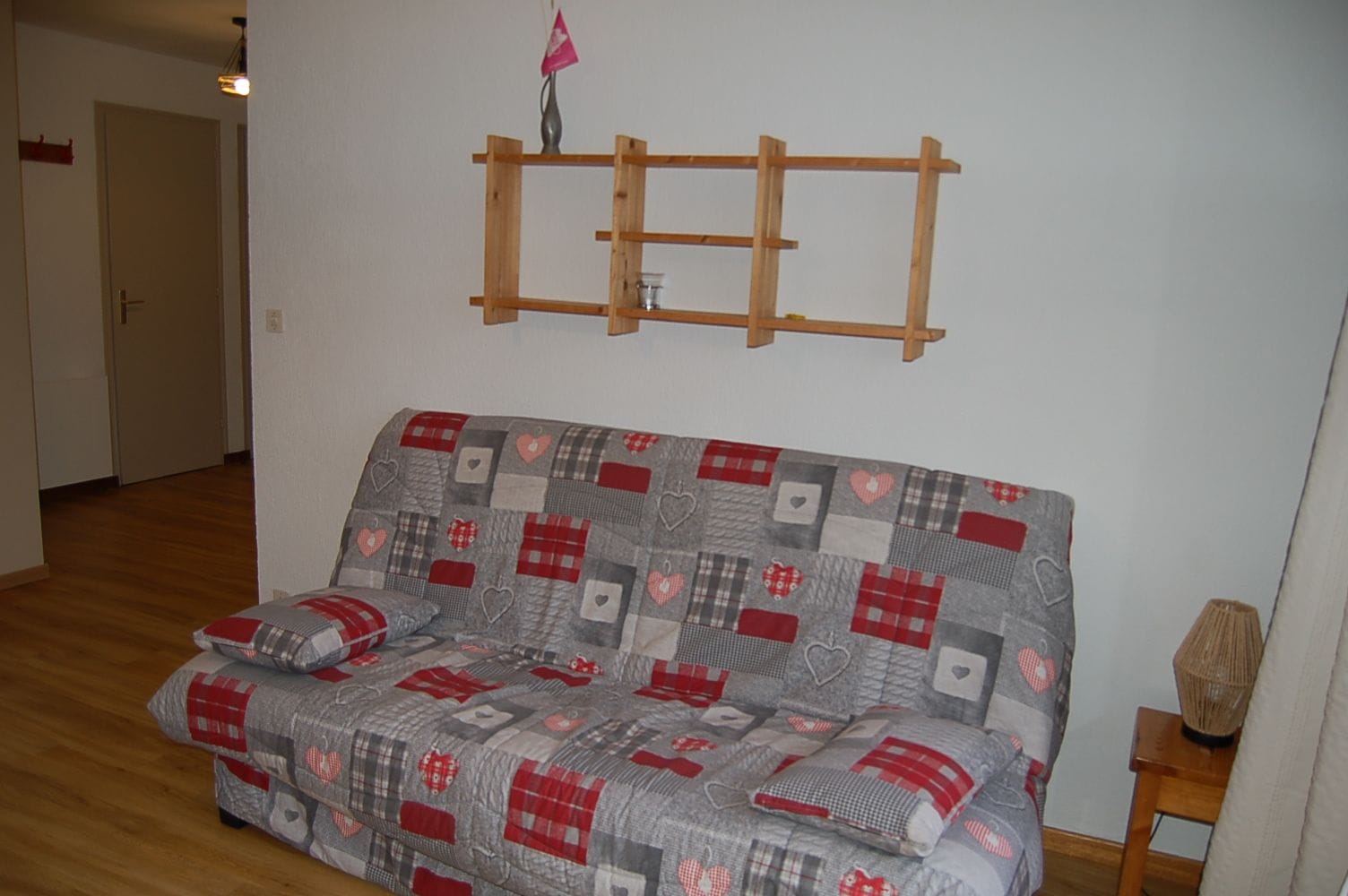 Ein Zimmer mit einer Couch, einem Holzregal und einer Lampe.