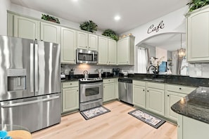 A modern kitchen with stainless steel appliances, light green cabinets, and a 'Cafe' sign above the counter. - 6BR Windsor Hills Home Near Disney With Pool (Kissimmee)