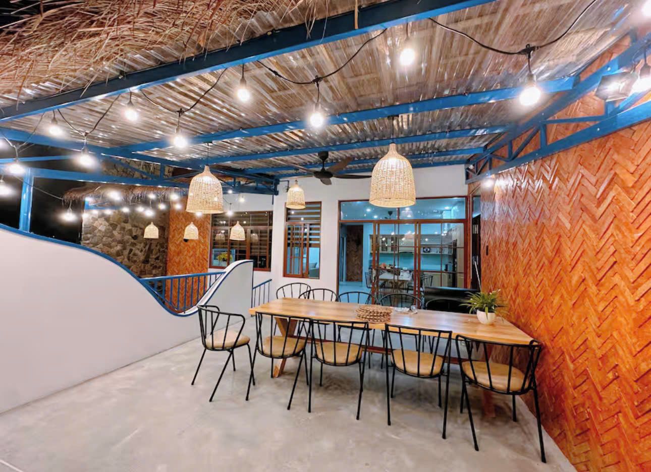 A dining area with a long wooden table, multiple chairs, hanging pendant lights, and a herringbone-patterned wall.