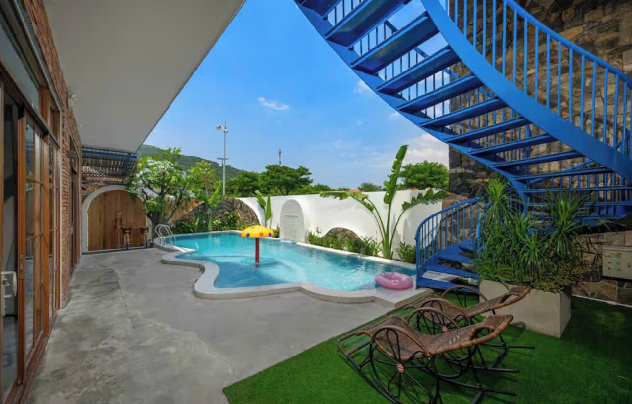 A swimming pool with a blue spiral staircase, surrounded by greenery and a clear sky.