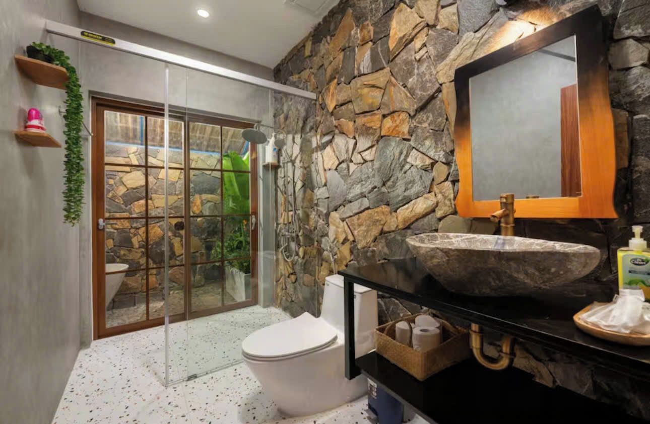 A bathroom with a stone wall, a large mirror, a sink, and a toilet.