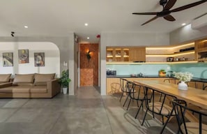 Cozinha moderna com bancada de madeira, área de jantar com mesa comprida e cadeiras, e ventilador de teto.