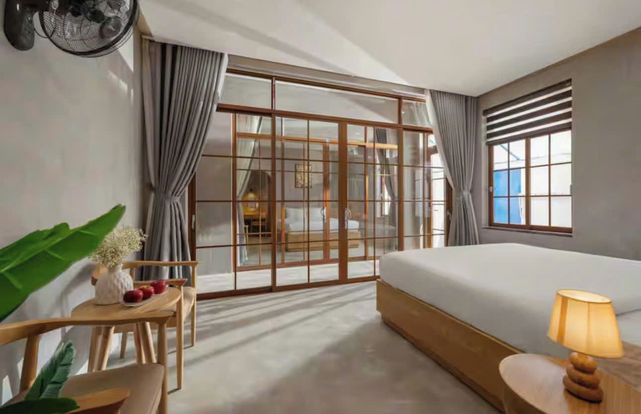 A hotel room with a bed, a desk, a chair, a lamp, and a large window with curtains.
