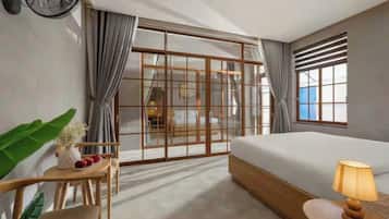 A hotel room with a bed, a desk, a chair, a lamp, and a large window with curtains.