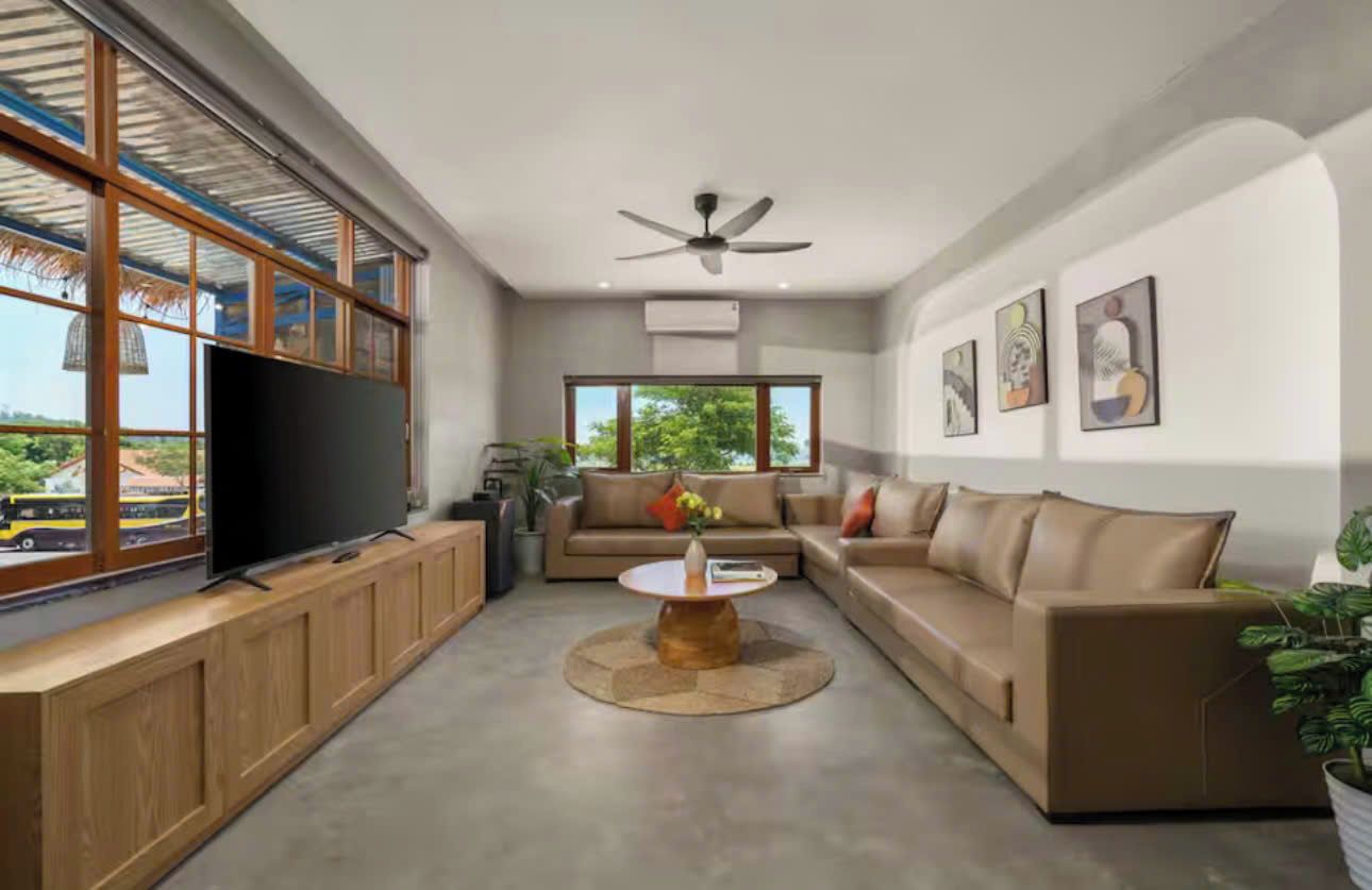 A modern living room with a large flat-screen TV, a ceiling fan, and a sofa set.