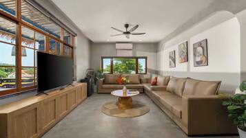 A modern living room with a large flat-screen TV, a ceiling fan, and a sofa set.